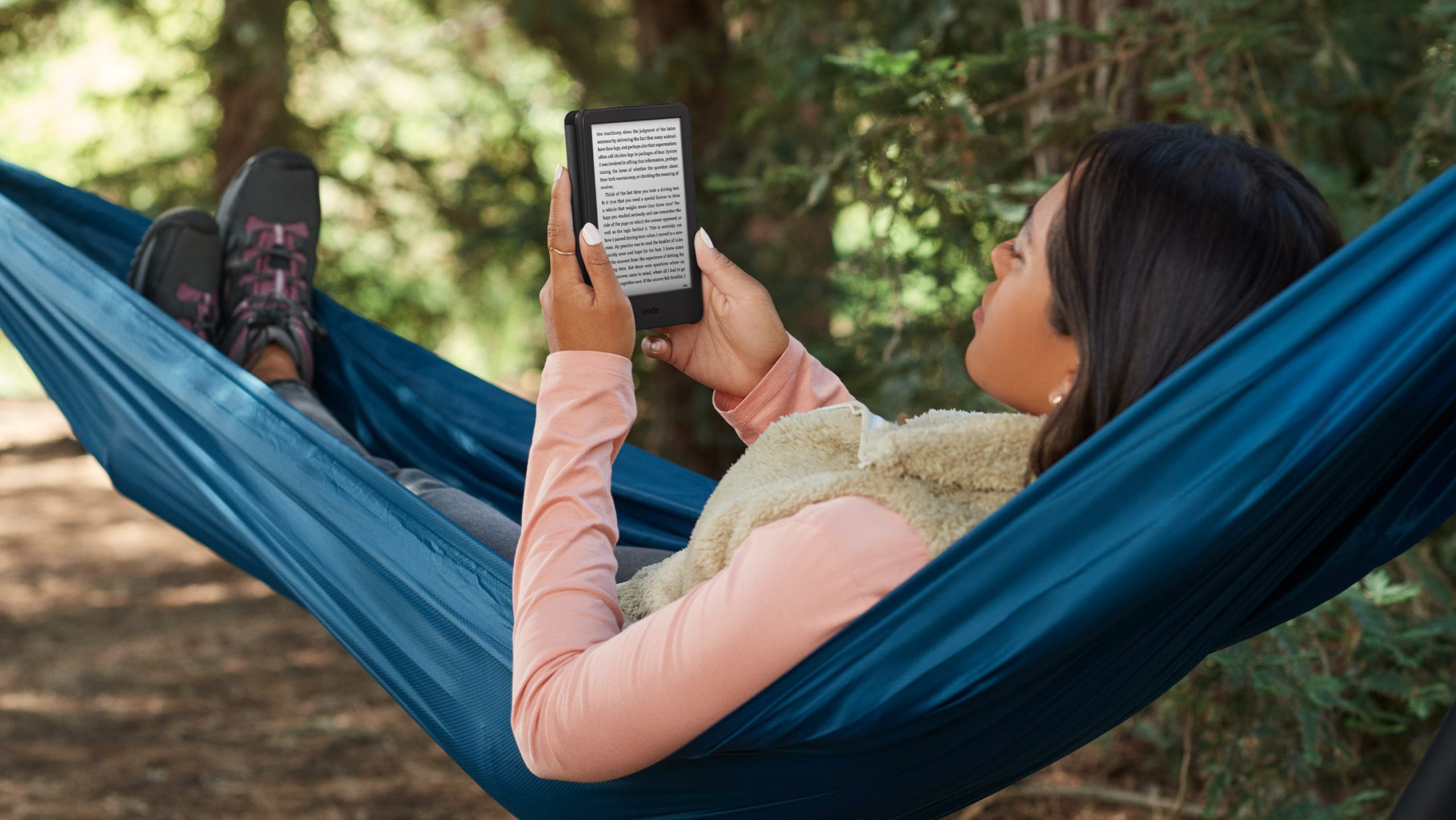 Women reading on a Kindle while laying in a hammock outside.